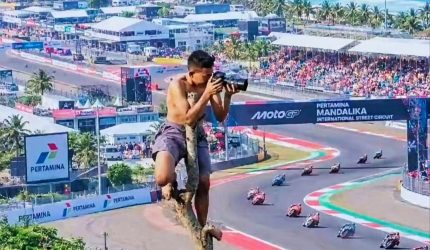 Warga memotret balapan MotoGP Mandalika 2026 dari atas pohon.